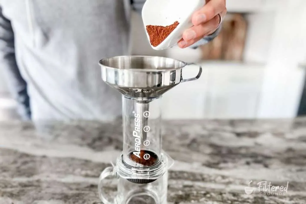 Coffee grounds being added to an AeroPress with a funnel