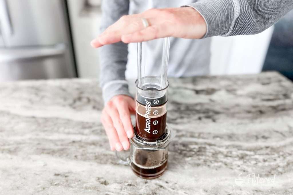 Home barista pressing coffee through an AeroPress into a glass coffee mug