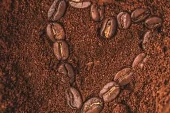 Coffee beans in the shape of a heart sitting in a pile of coffee grounds