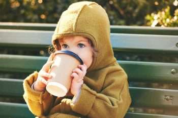 Small child drinking coffee on a park bench