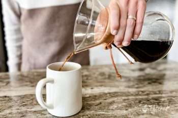 Home barista pouring freshly brewed coffee from a Chemex into a coffee mug