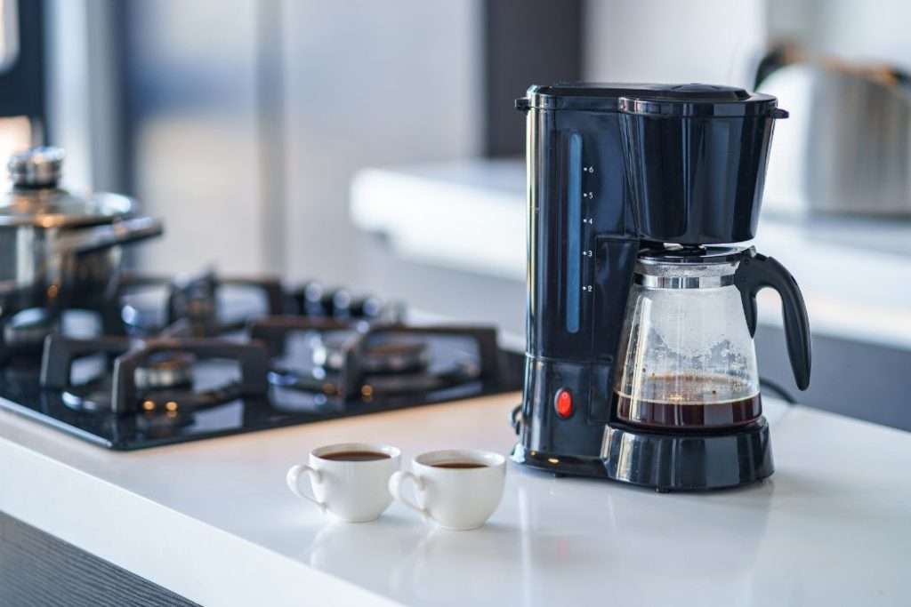Auto-drip coffee machine sitting next to two cups of coffee on a kitchen island