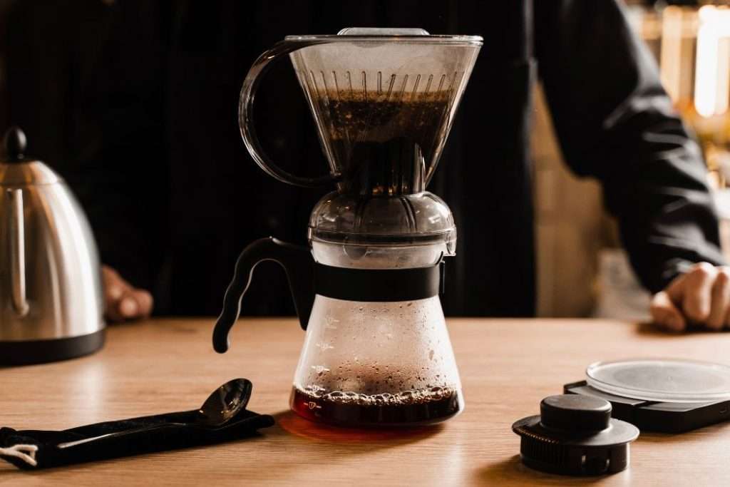 Clever Dripper brewing coffee into a glass carafe with a home barista in the background