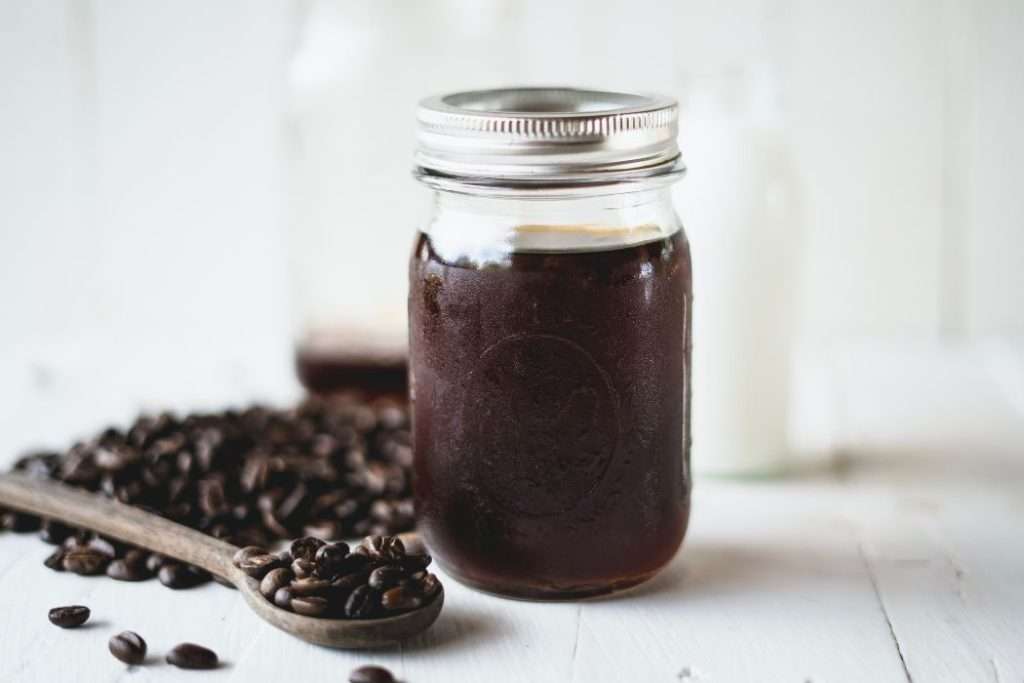 Mason jar filled with cold brew concentrate sitting next to a pile of coffee beans