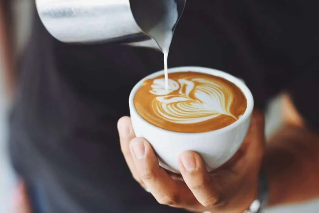 Professional barista using a milk pitcher to create latte art on a cappuccino