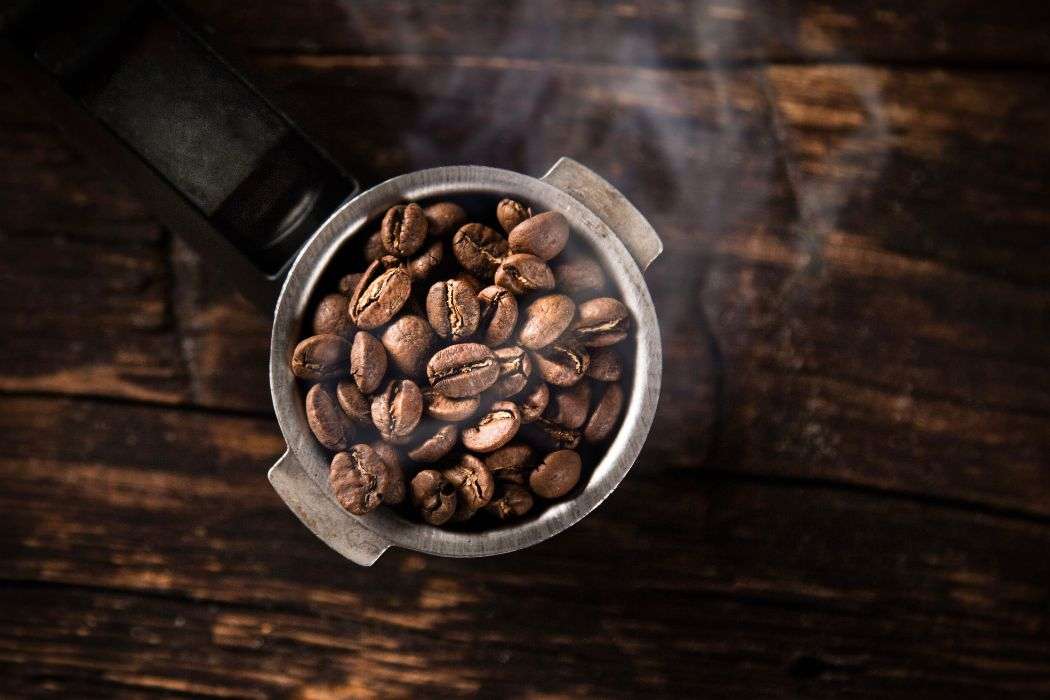 Portafilter filled with roasted coffee beans covered by a faint haze of smoke