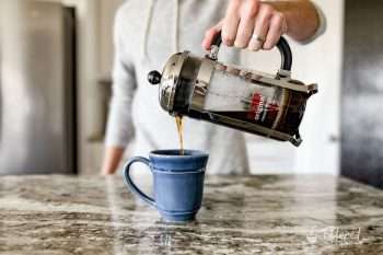 Home barista pouring coffee from a French press into a blue coffee mug