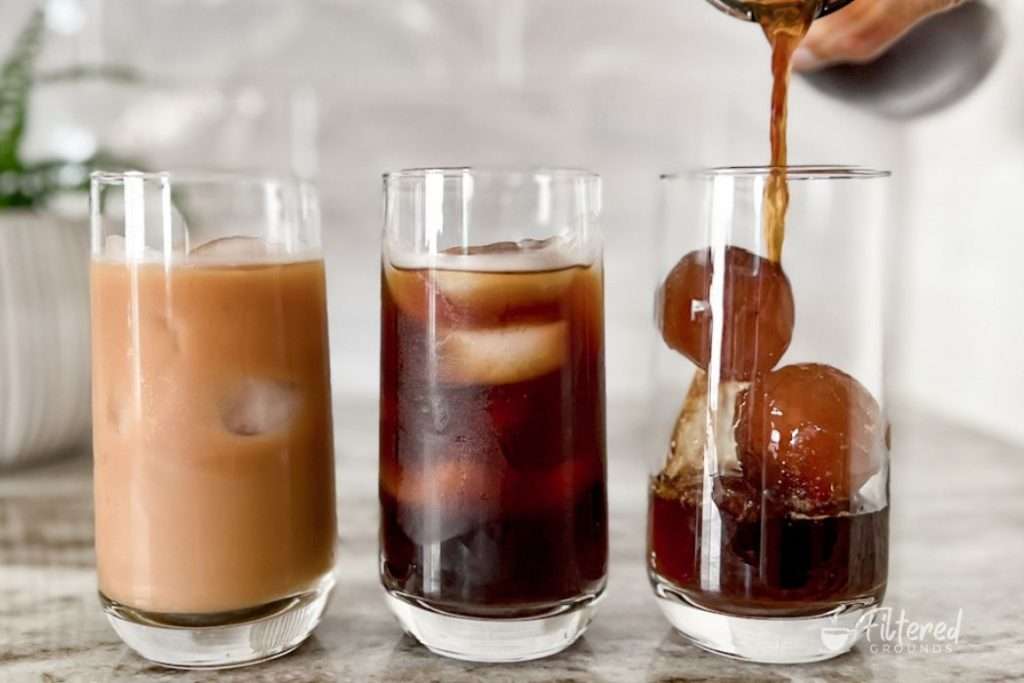Three glasses of cold brew coffee, one with creamer, one without creamer, and one with coffee ice cubes