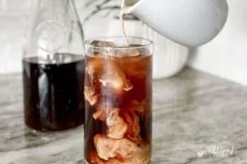 Creamer being poured into a glass of iced cold brew coffee