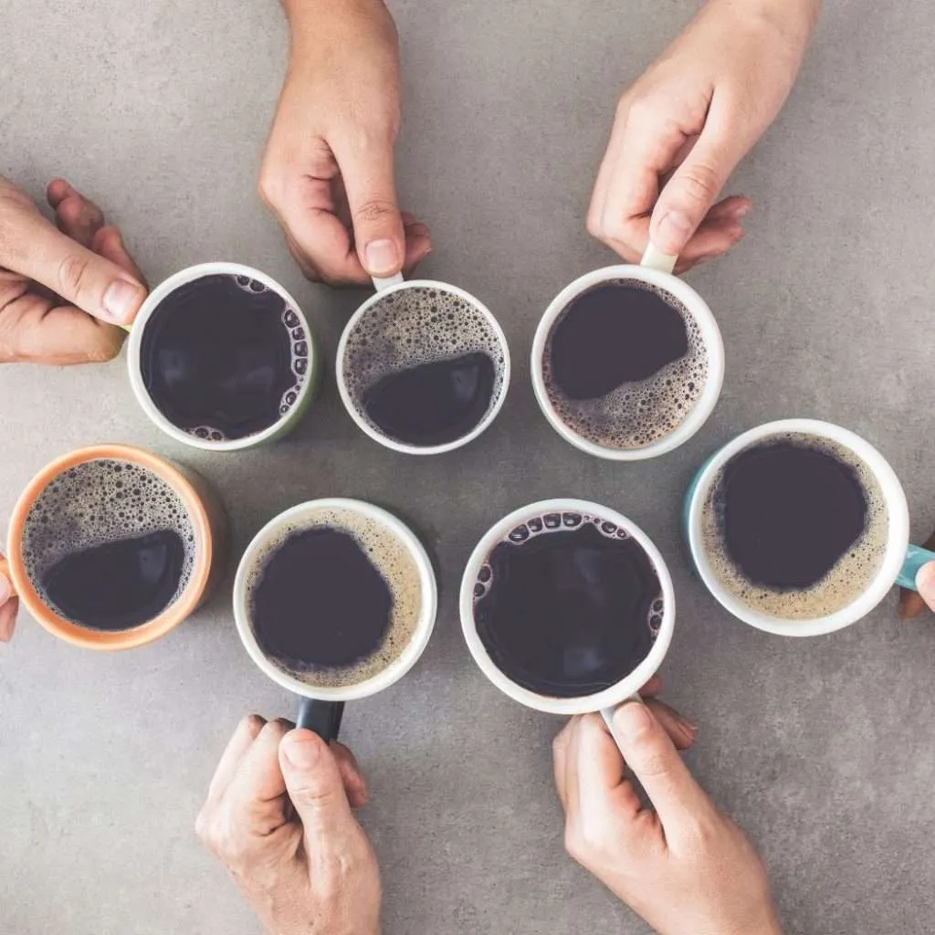 Seven coffee cups sitting on a table being held by seven different hands
